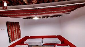 Une pièce comprenant un lit, deux oreillers, un tapis rayé rouge et blanc et un tissu rouge et blanc à motifs suspendu.