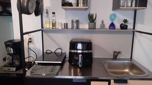 Ett kök med en kaffebryggare, en brödrost, en vattenkokare, ett handfat och hyllor med diverse föremål.