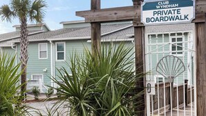 A private boardwalk leading to Club Wyndham, with a wooden railing and palm trees in the foreground.