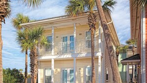 A two-story building with a balcony, surrounded by palm trees and a garden.
