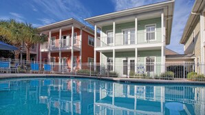 A two-story building with balconies, a swimming pool, and a fenced area with lounge chairs.