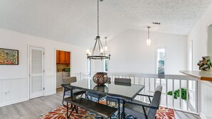 Zona pranzo con tavolo in vetro, panche e un lampadario. Sul pavimento, un tappeto colorato, e sullo sfondo si intravede una cucina.