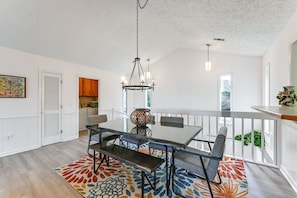 A dining area with a glass table, benches, and a chandelier. There is a colorful rug on the floor, and a kitchen area is visible in the background. - Deck & Community Perks: Sky Valley Home! (Dillard)