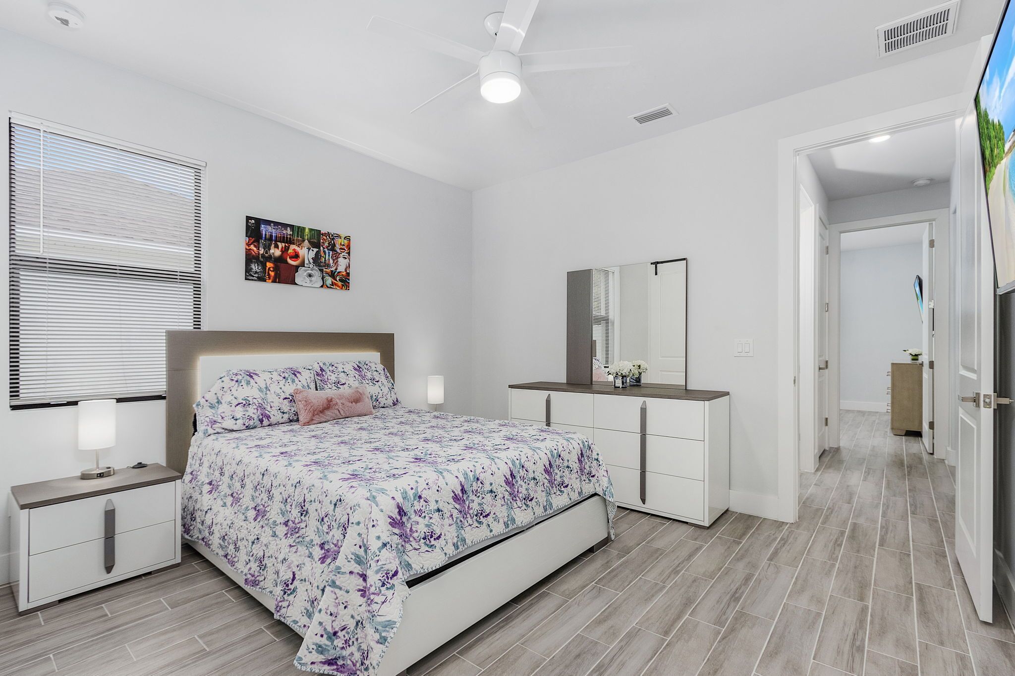 Un dormitorio con cama, mesitas de noche, cómoda, espejo y ventilador de techo.