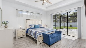 Ein Schlafzimmer mit Bett, Nachttischen, einer kleinen Sitzecke, einer blauen Bank, einem Deckenventilator und einer großen Glasschiebetür, die auf eine Terrasse im Freien führt.