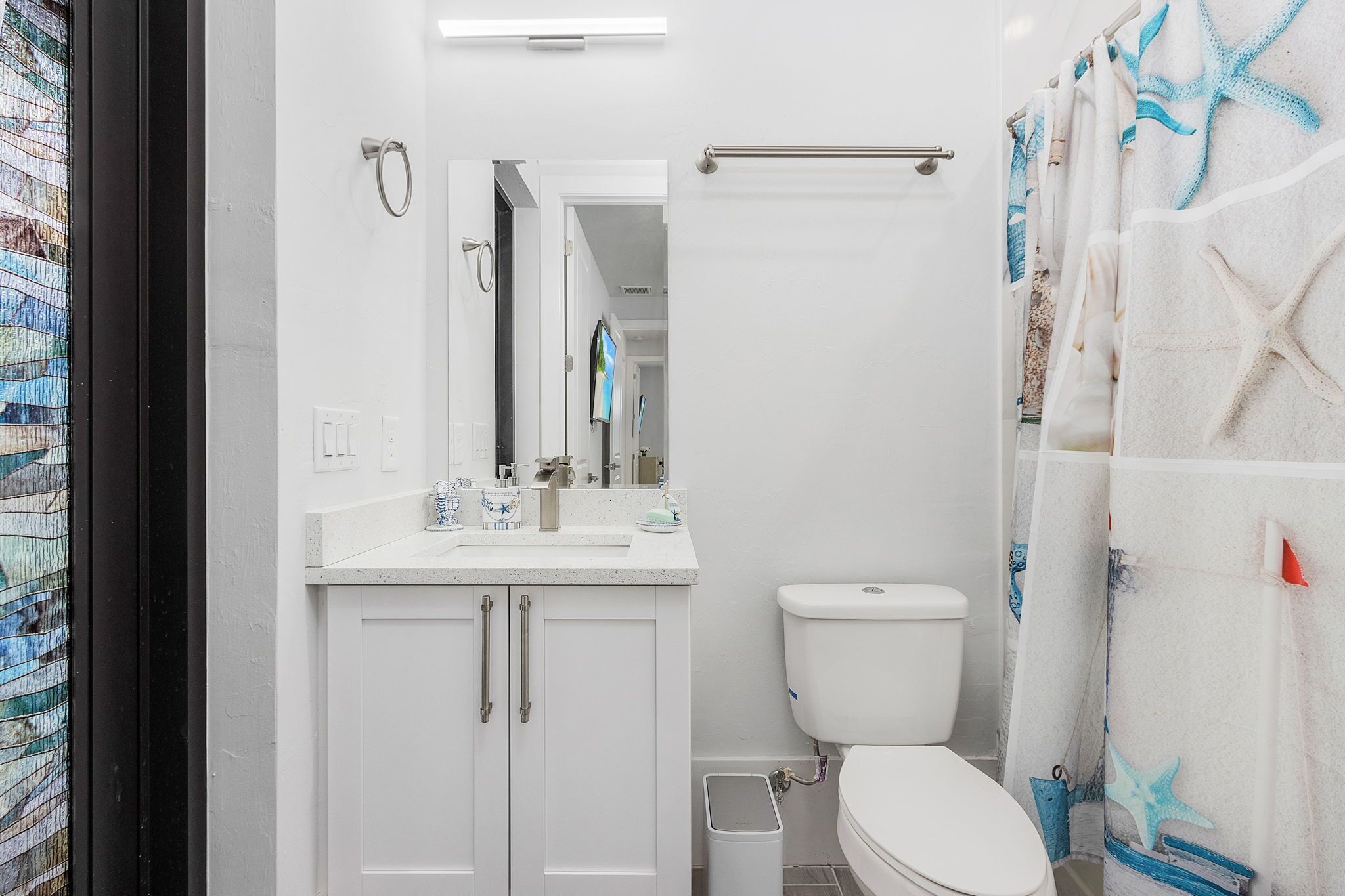 Un baño moderno con lavamanos, espejo y retrete blancos. Cuenta con una cortina de ducha con diseño de estrella de mar.