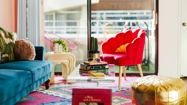 A modern living room with a blue sofa, a red chair, and a small table with books and a cactus. - Palme Diem! Condo Close to Downtown! (Palm Springs)