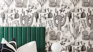 A bedroom with a green upholstered headboard, a patterned bedspread, and a nightstand with a lamp and decorative items. - Palme Diem! Condo Close to Downtown! (Palm Springs)
