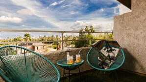 A balcony with two chairs and a table, a clear view of the sky, and a building in the background. - Palme Diem! Condo Close to Downtown! (Palm Springs)