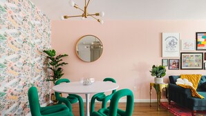 A dining area with a round table, green chairs, a mirror, and a wall with colorful artwork. - Palme Diem! Condo Close to Downtown! (Palm Springs)
