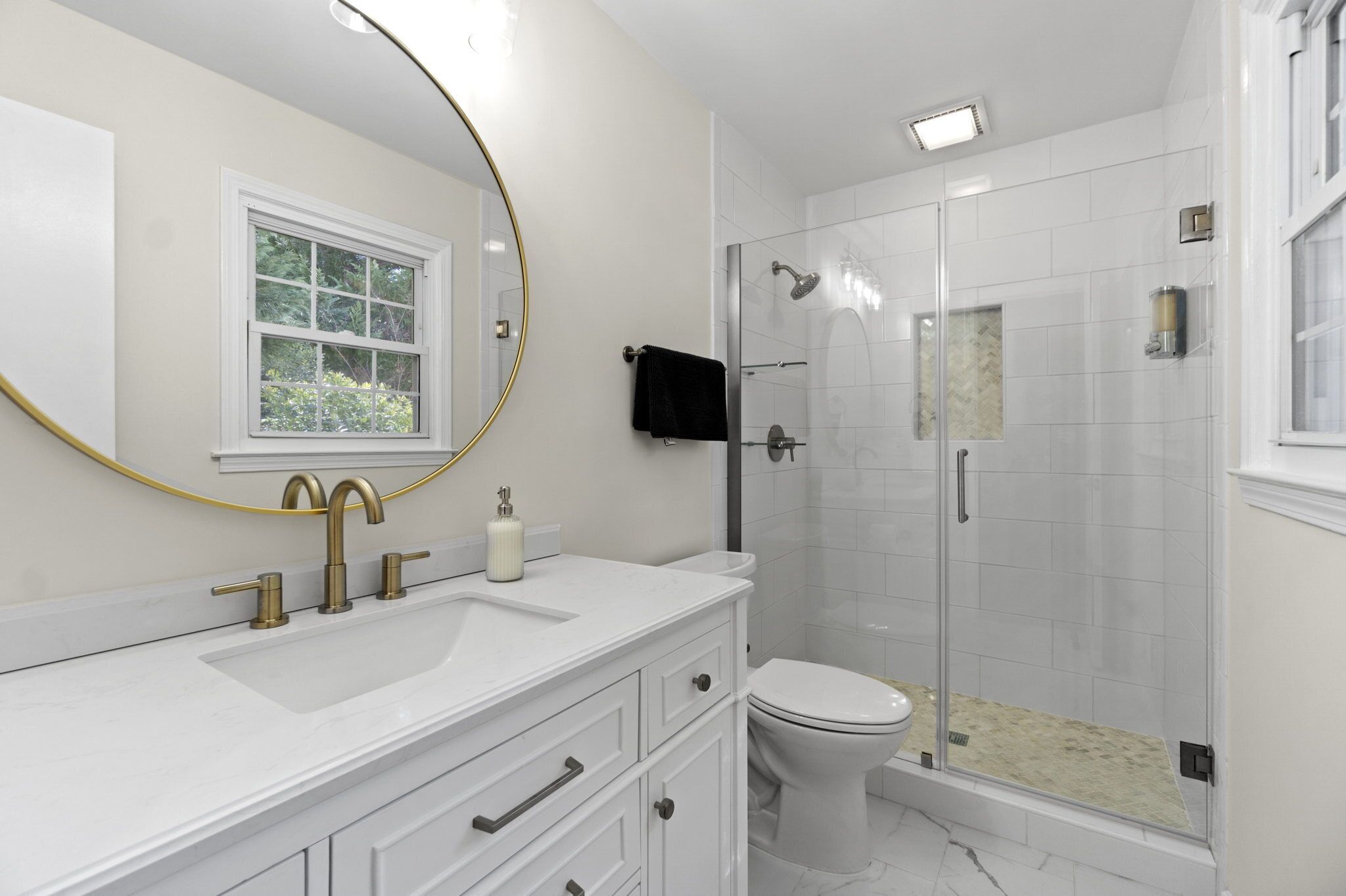 Een moderne badkamer met een wit wastafelmeubel, een grote spiegel, een toilet en een douche met glazen wanden.
