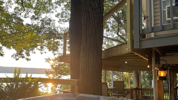 Een hottub met waterval, omringd door een houten terras en met uitzicht op een waterpartij.