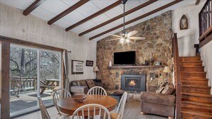 A cozy living room with a stone fireplace, wooden ceiling beams, and a TV mounted above it.