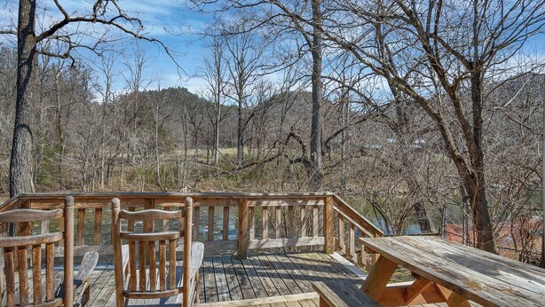 A wooden deck with benches and picnic tables overlooking a forested area.