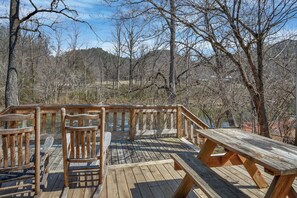 Une terrasse en bois, dotée de bancs et de tables de pique-nique, qui offre une vue sur une zone boisée.