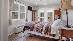 A bedroom with a bed, a ceiling fan, a window with curtains, a radiator, and a wooden floor.