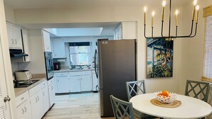 A modern kitchen with white cabinets, a built-in oven, and a refrigerator. There is a dining area with a round table and chairs, and a painting on the wall. - Have it all at this beautiful waterfront Homosassa home close to all amenities. (Homosassa)