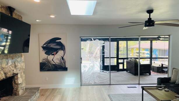 A modern living room with a stone fireplace, a large painting, and a view through glass doors to an outdoor patio. - Have it all at this beautiful waterfront Homosassa home close to all amenities. (Homosassa)