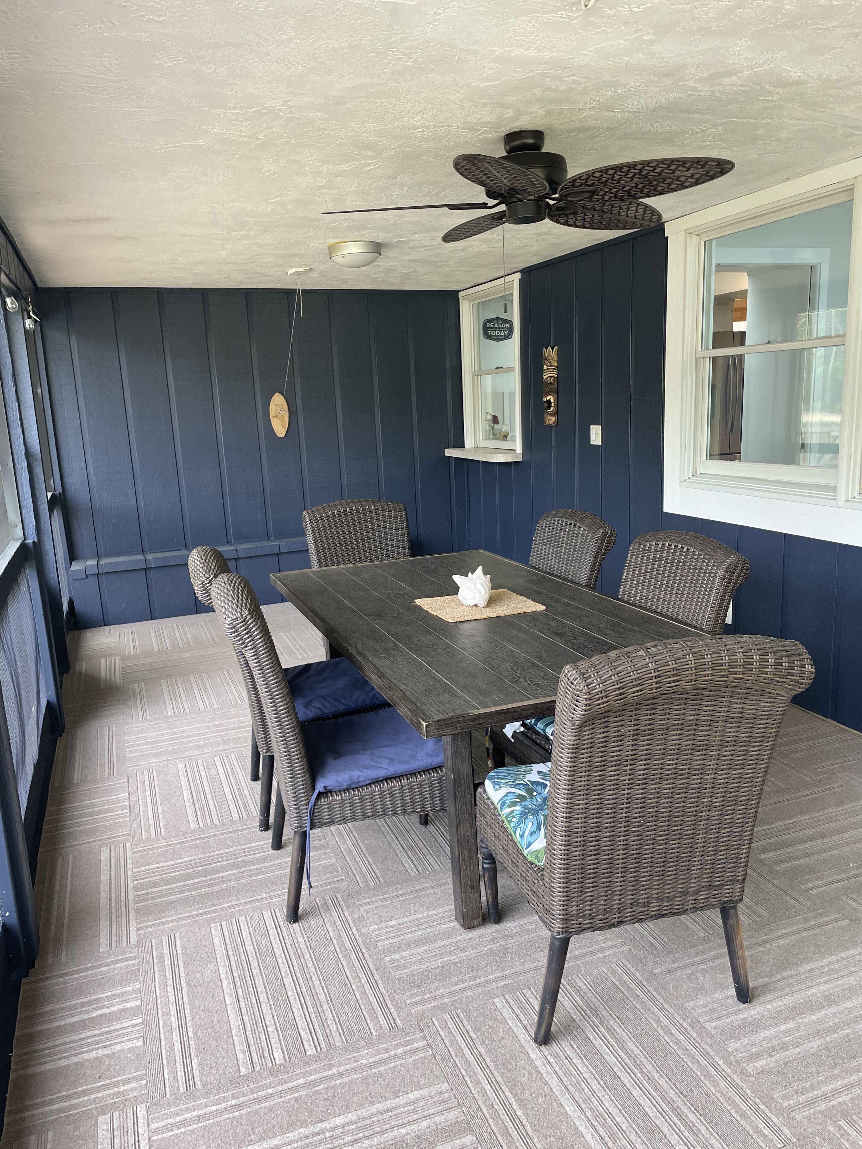 A dining area with a dark wooden table, wicker chairs, and a ceiling fan.
