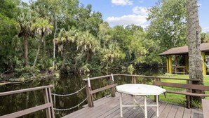 A wooden deck with a table and chairs overlooking a body of water surrounded by trees. - Have it all at this beautiful waterfront Homosassa home close to all amenities. (Homosassa)