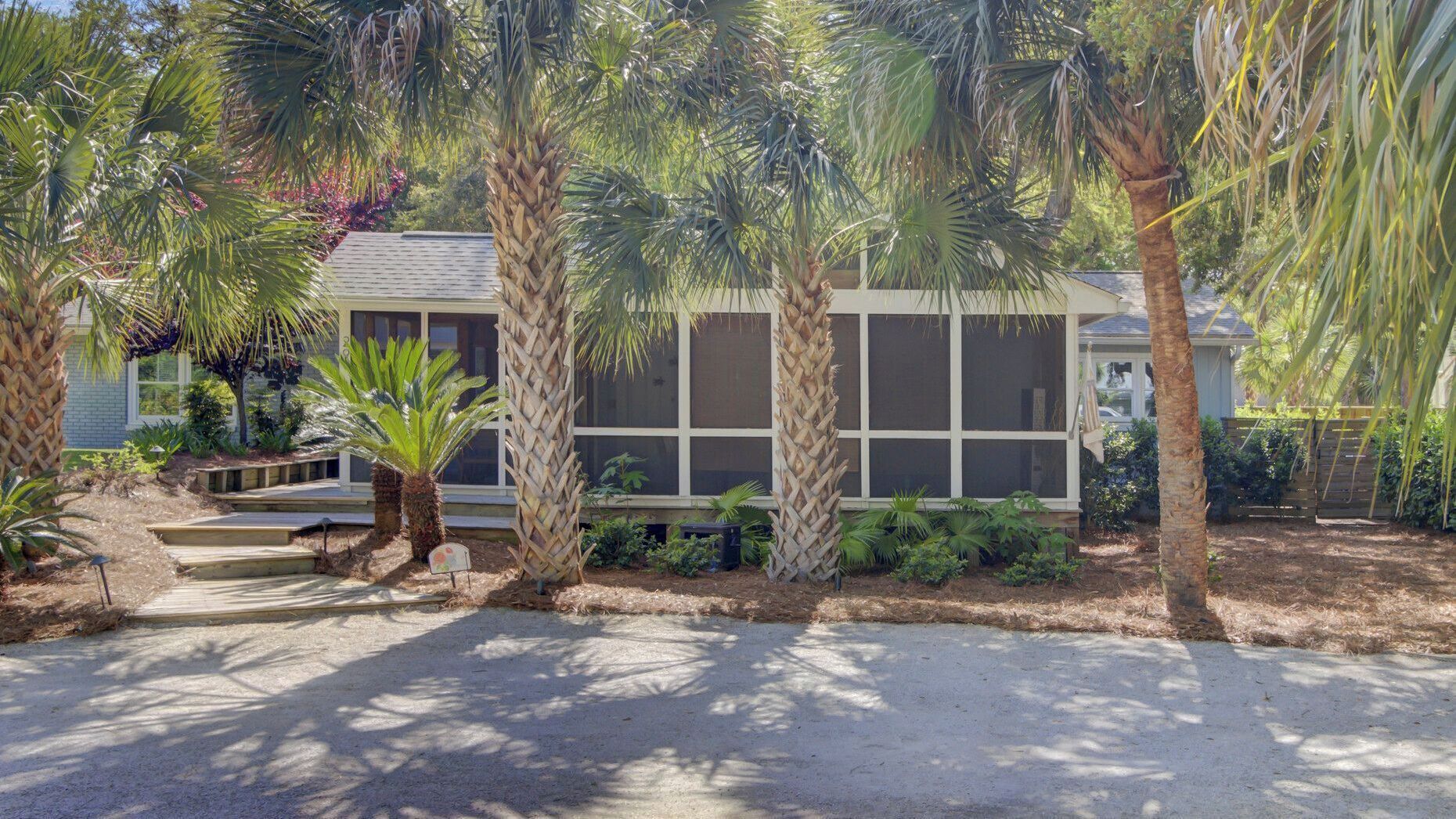 A house with a screened porch, palm trees, and a gravel driveway.