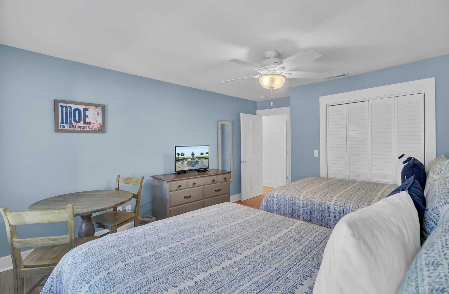 A bedroom with two beds, a desk, a chair, a television, and a ceiling fan.