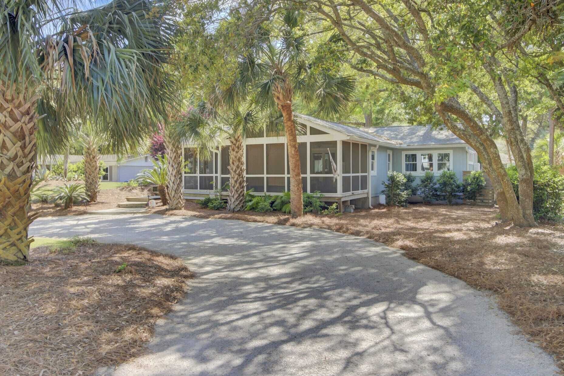 A single-story house with a covered porch, surrounded by mature trees and a paved driveway.