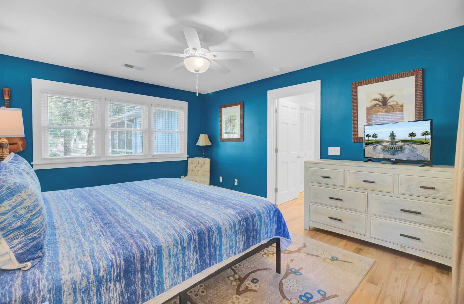 A bedroom with a bed, a dresser, a ceiling fan, a window, and a door.