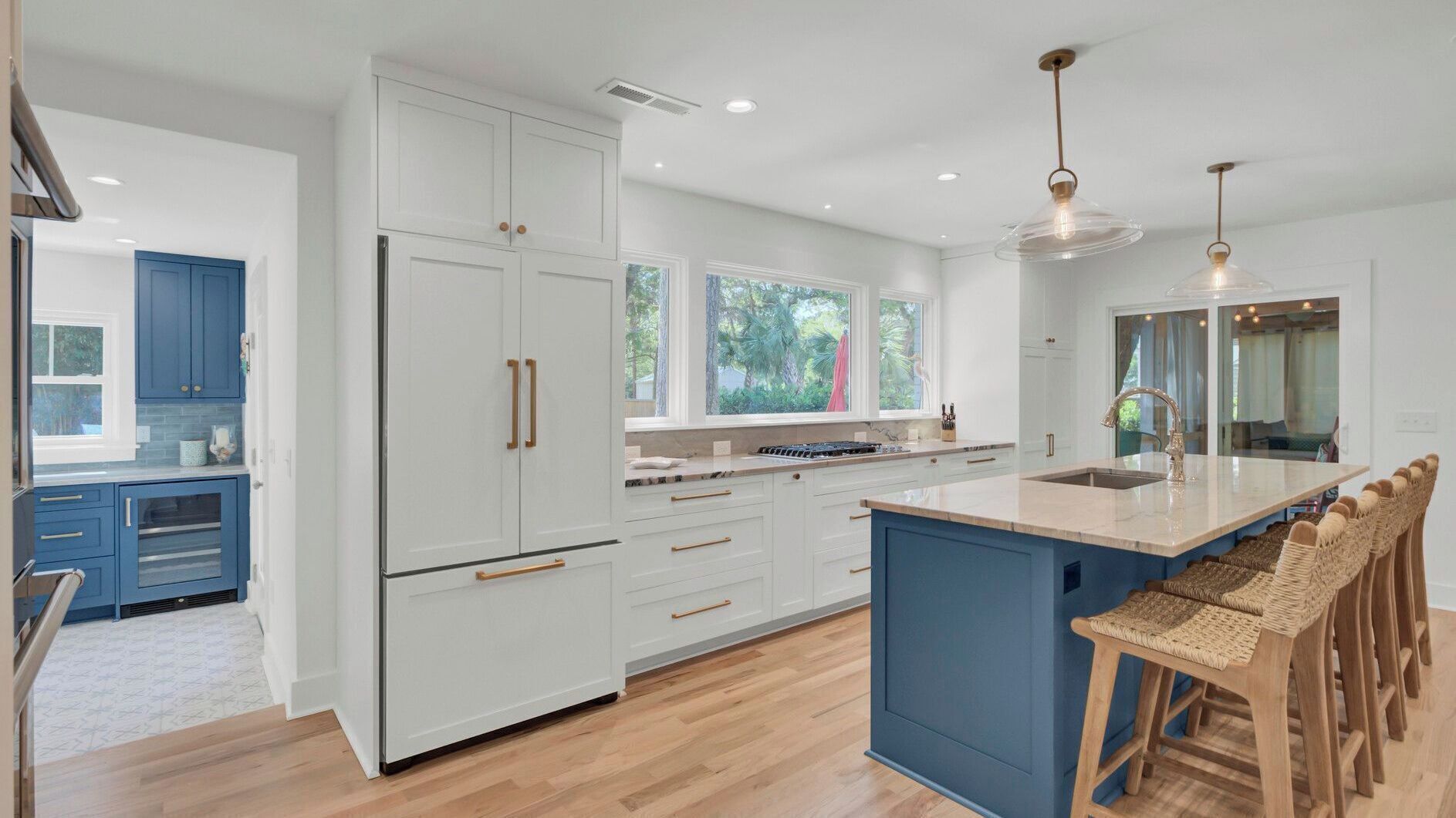 A modern kitchen with white cabinetry, a large island with bar stools, and a view of the outdoors through windows.