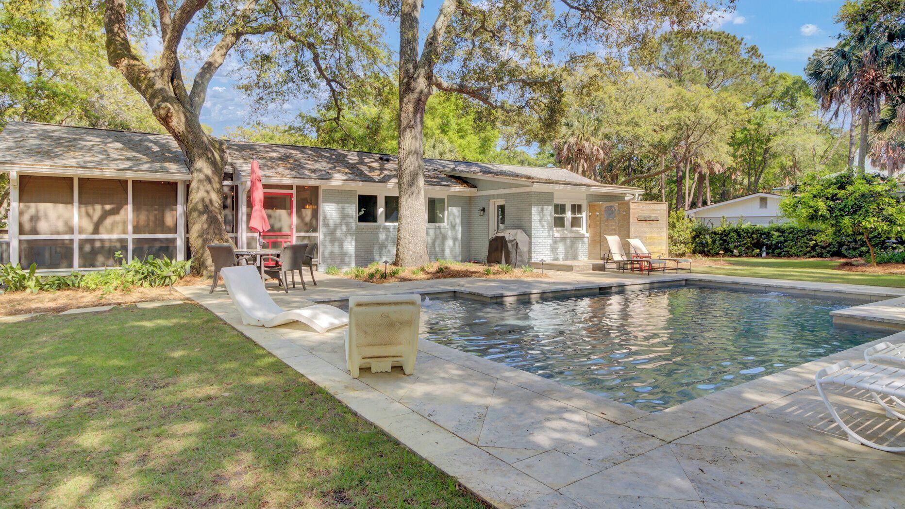 A residential property with a swimming pool, outdoor seating, and a covered patio area.