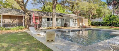 A residential property with a swimming pool, outdoor seating, and a covered patio area.