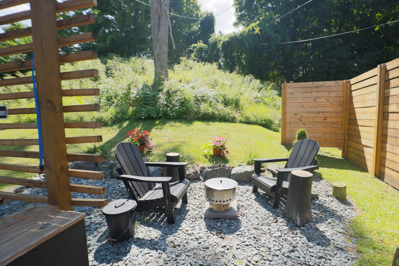 Un patio con sillas tipo Adirondack, una fogata y un cerco de madera.