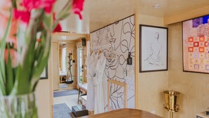 Une pièce avec un plancher en bois, une table en bois, un vase rempli de fleurs et un mur orné d’œuvres d’art encadrées.