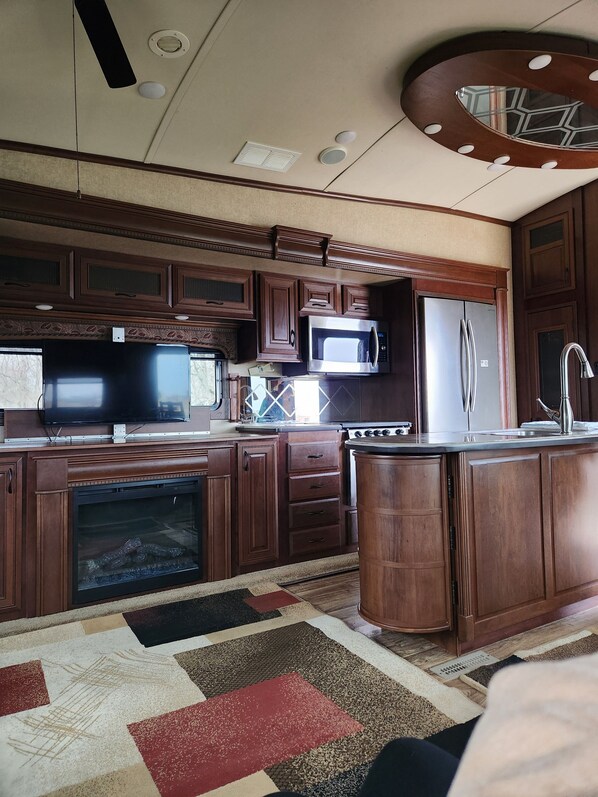 A spacious kitchen with dark wooden cabinets, stainless steel appliances, and a large island. - Cozy RV for the Solar Eclipse (Fort Jennings)