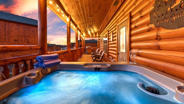 Una cabaña de madera con jacuzzi, sillas de descanso y vistas al atardecer.