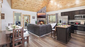 Amplia sala de estar con chimenea, techo de madera y cocina equipada con electrodomésticos modernos.
