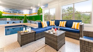 Un área junto a la piscina con un sofá azul, mobiliario de mimbre y un mural que representa un oso.