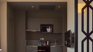A modern living room with a sofa, a coffee table, and a book. In the background, there is a kitchen with a microwave, a coffee machine, and a refrigerator. - M Suite Hotel (Algiers)