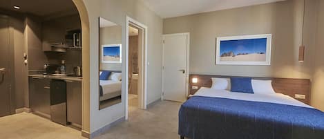 A modern hotel room with a bed, a desk, and a kitchenette.