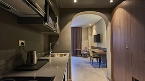 A modern kitchen with a built-in stove, a sink, and a microwave. There is a dining area with a table and chairs visible through an archway. - M Suite Hotel (Algiers)