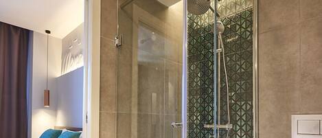 A modern bathroom with a glass-enclosed shower, a white toilet, and a bed with blue pillows.