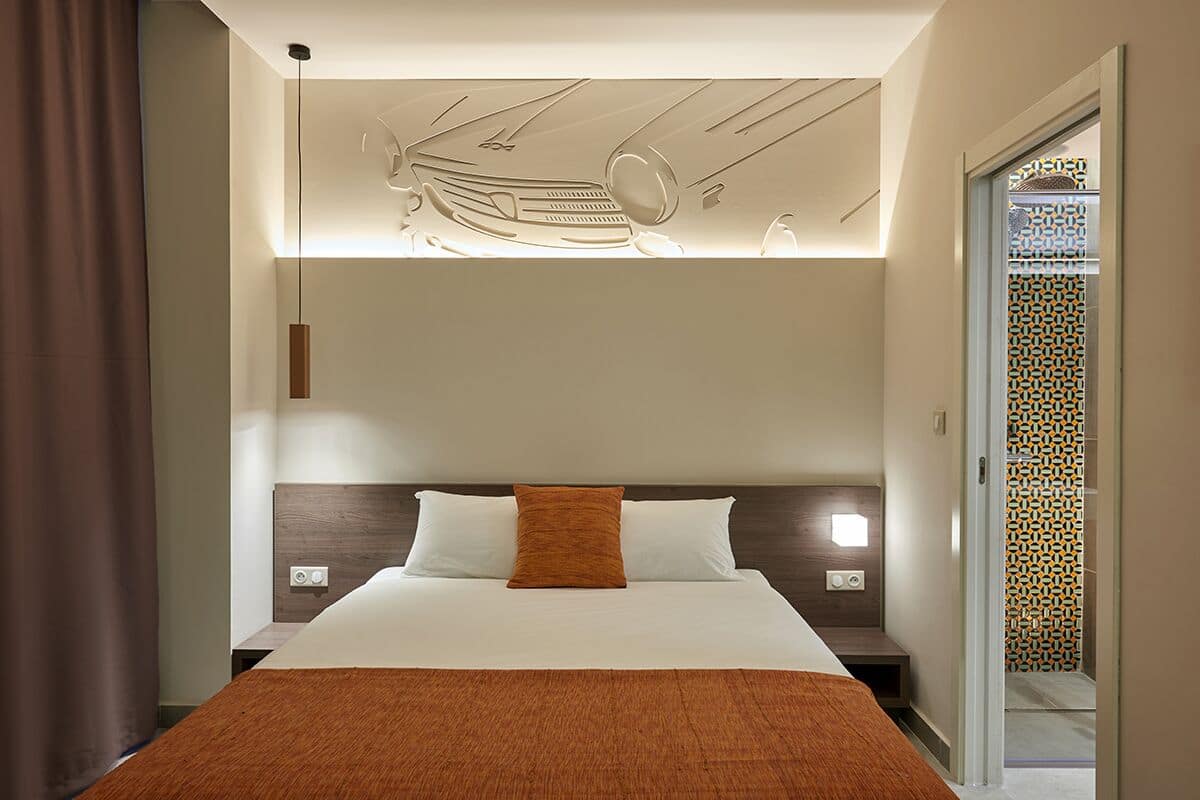 Una habitación de hotel moderna con una cama grande, cabecera con iluminación integrada, mesita de noche y diseño de pared estampado.