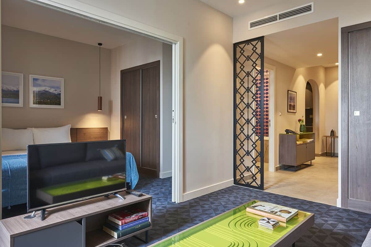 Una habitación de hotel moderna con sofá, televisor y una mesa de comedor con libros.