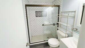 Ein modernes Badezimmer mit weißen Fliesen, einer Duschkabine aus Glas, einer weißen Toilette und einer Glasregaleinrichtung.