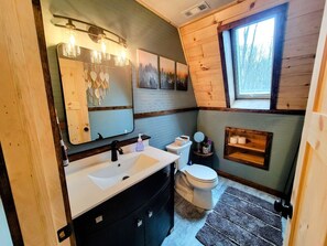 A compact bathroom with a wooden sloped ceiling, a white sink, a toilet, and a small window.