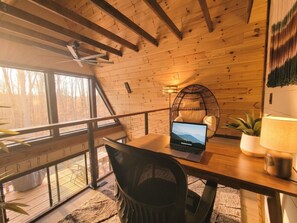 A wooden interior with a laptop on a table, a chair, a hanging light fixture, and a view through large windows. - Gorgeous New A-Frame w/ Sauna & Gameroom - Minutes to Pools, Golf and Skiing (Bellaire)