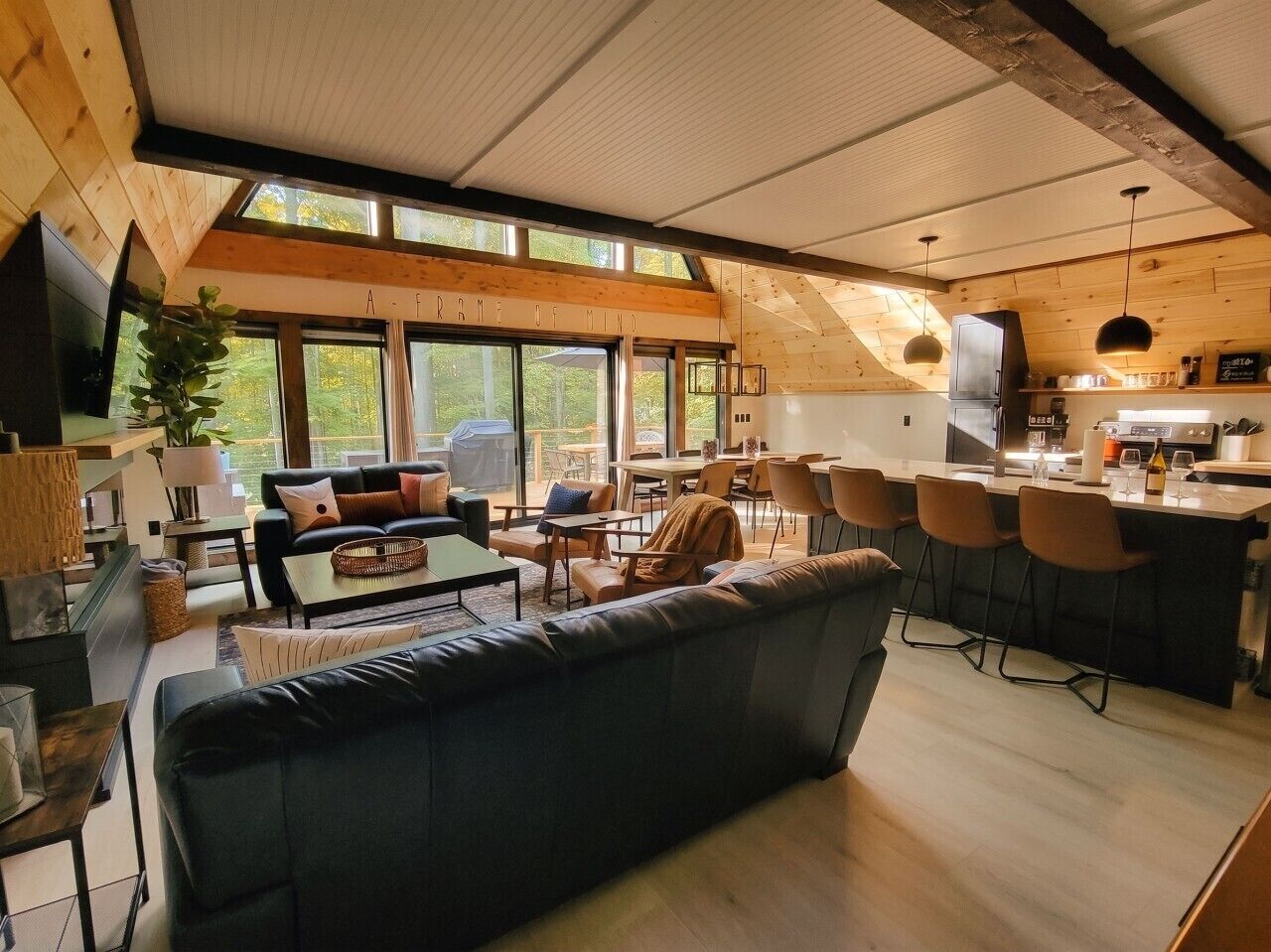 Amplia sala de estar con un sofá grande, una mesa de comedor y sillas, un área de cocina con refrigerador, y ventanas grandes que permiten la entrada de luz natural.