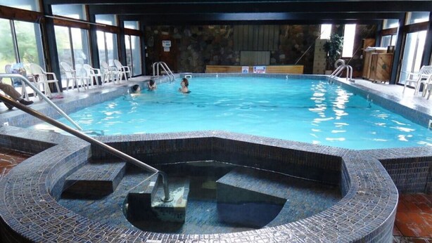 Een binnenzwembad met een jacuzzi met mozaïektegels, omringd door ligbedden en een stenen muur.