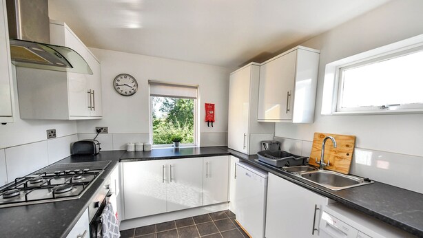 Een moderne keuken met witte kasten, een gasfornuis, een spoelbak en een vaatwasser.