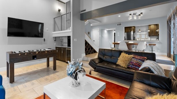 A modern living room with a foosball table, a flat-screen TV, a sofa, and a kitchen area in the background.